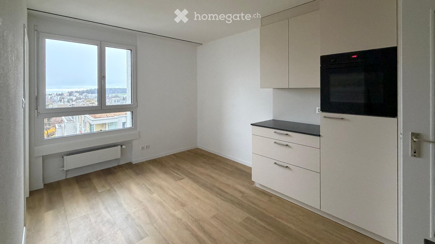 Modern kitchen with light-colored cabinets, a built-in oven, and a large window offering a city view.