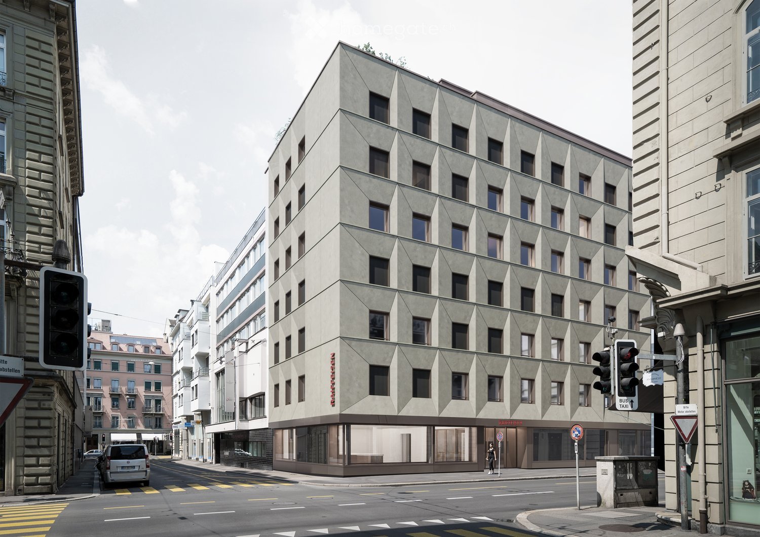 Modern multi-story building with geometric facade and numerous windows, located at a street corner with traffic signals and pedestrian crossing.