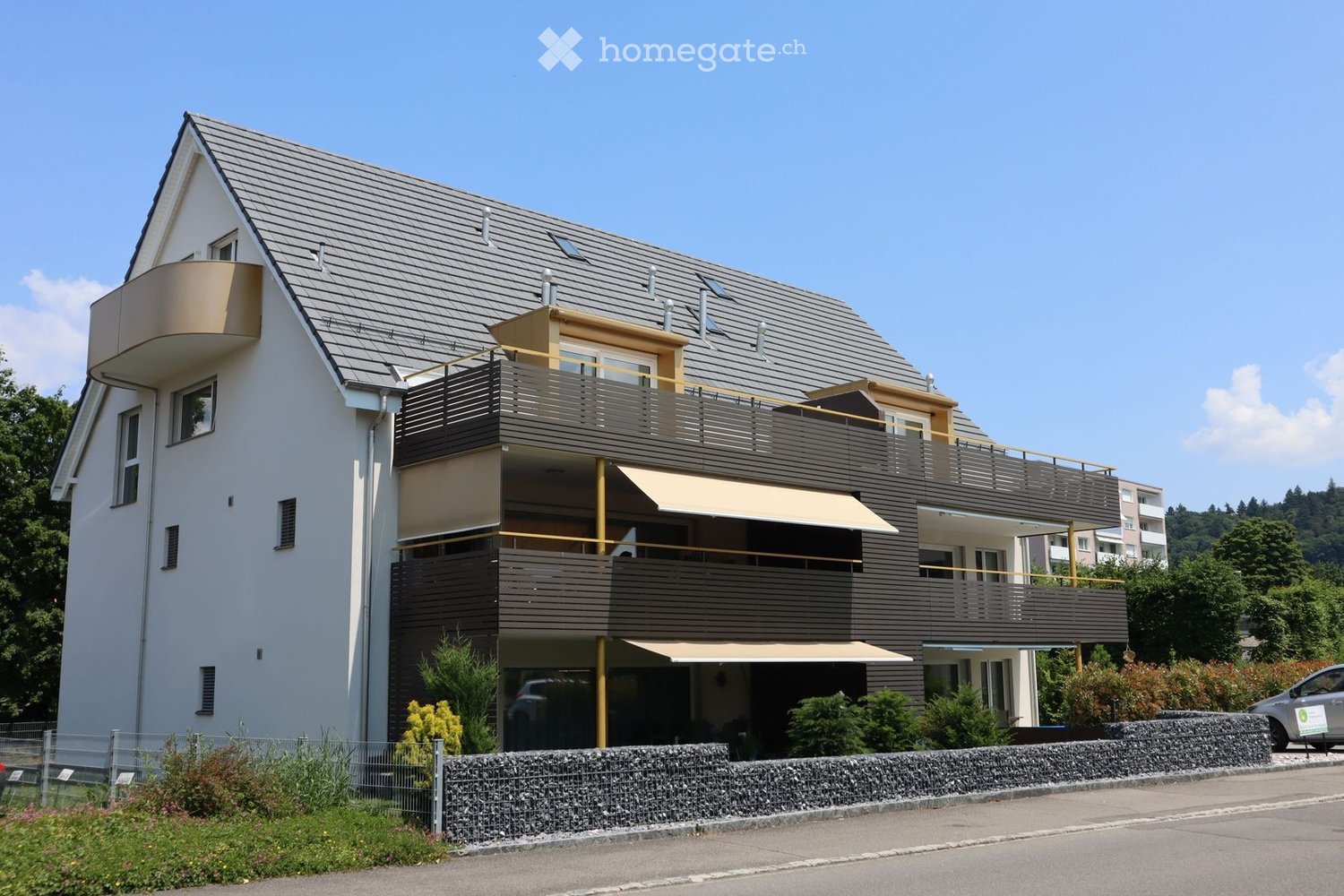 2 story house, white exterior, gray roof, multiple balconies, awnings, garden, car parked