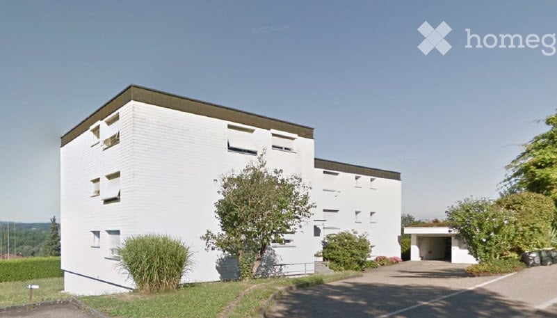 Modern white building with flat roof, multiple windows, and a small garage entrance.