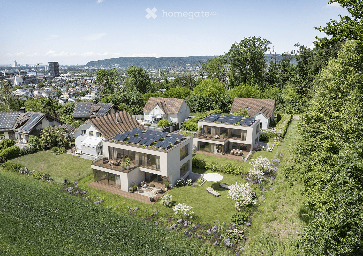 House. Aerial view of a modern, multi-story house with solar panels on the roof, surrounded by a well-maintained garden with lounge chairs, a table, and an umbrella. The house features large windows and a raised ground floor, with a cityscape visible in t
