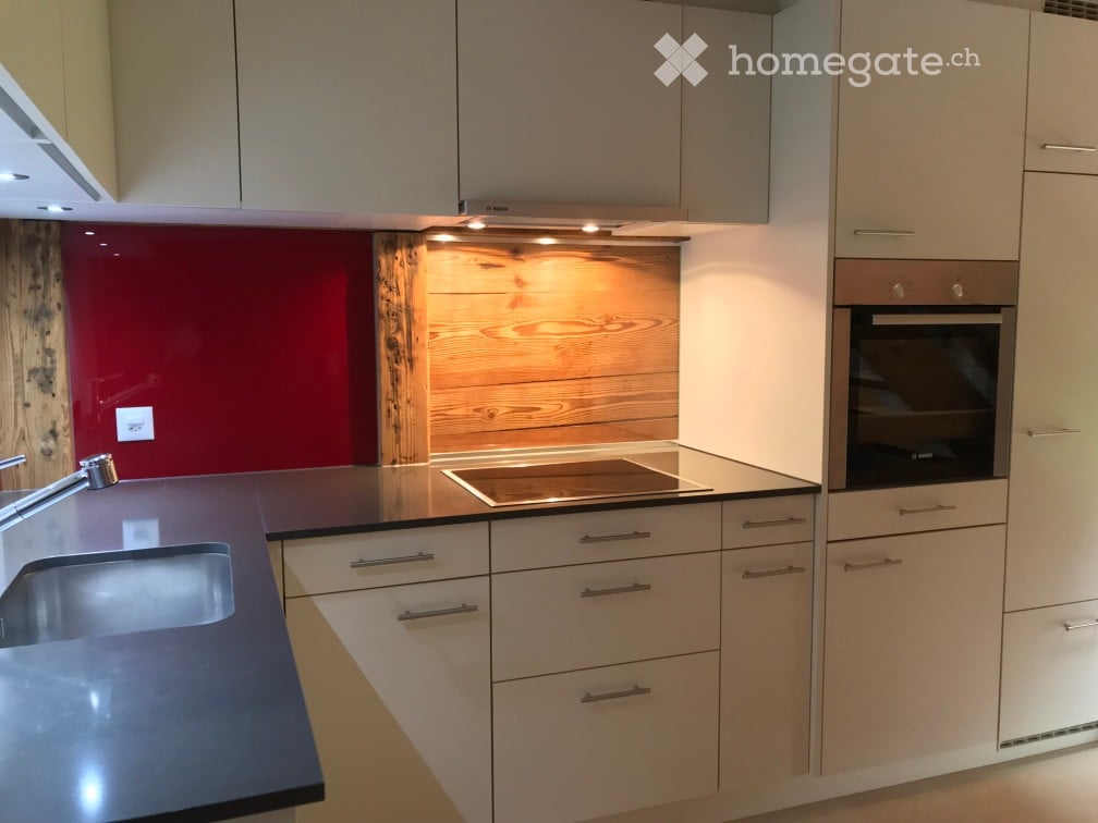 modern kitchen with white cabinets, black countertops, induction stove, oven, sink, faucet, wooden backsplash, red wall