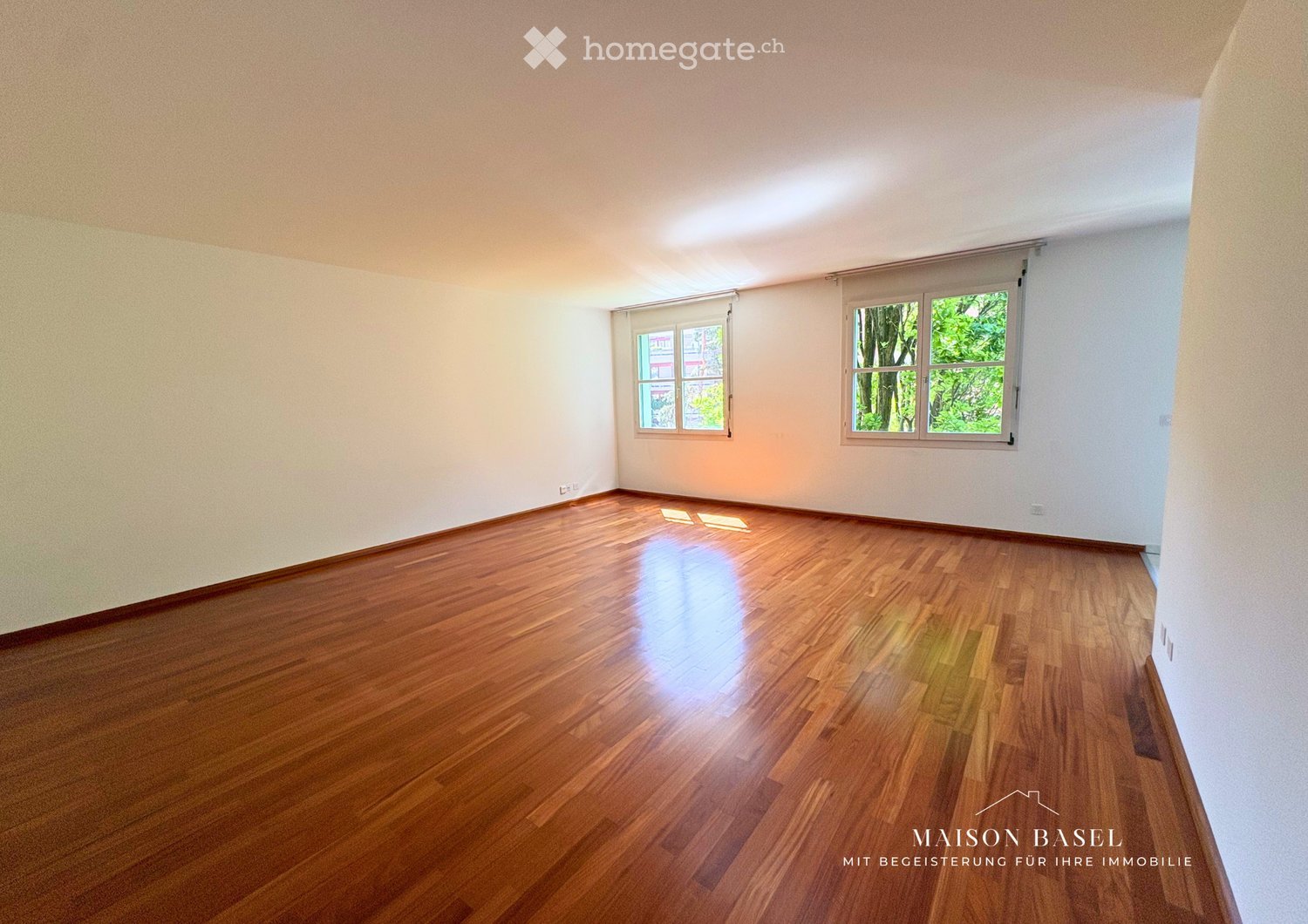 Empty room with wooden flooring and white walls, featuring two windows with blinds and natural light.
