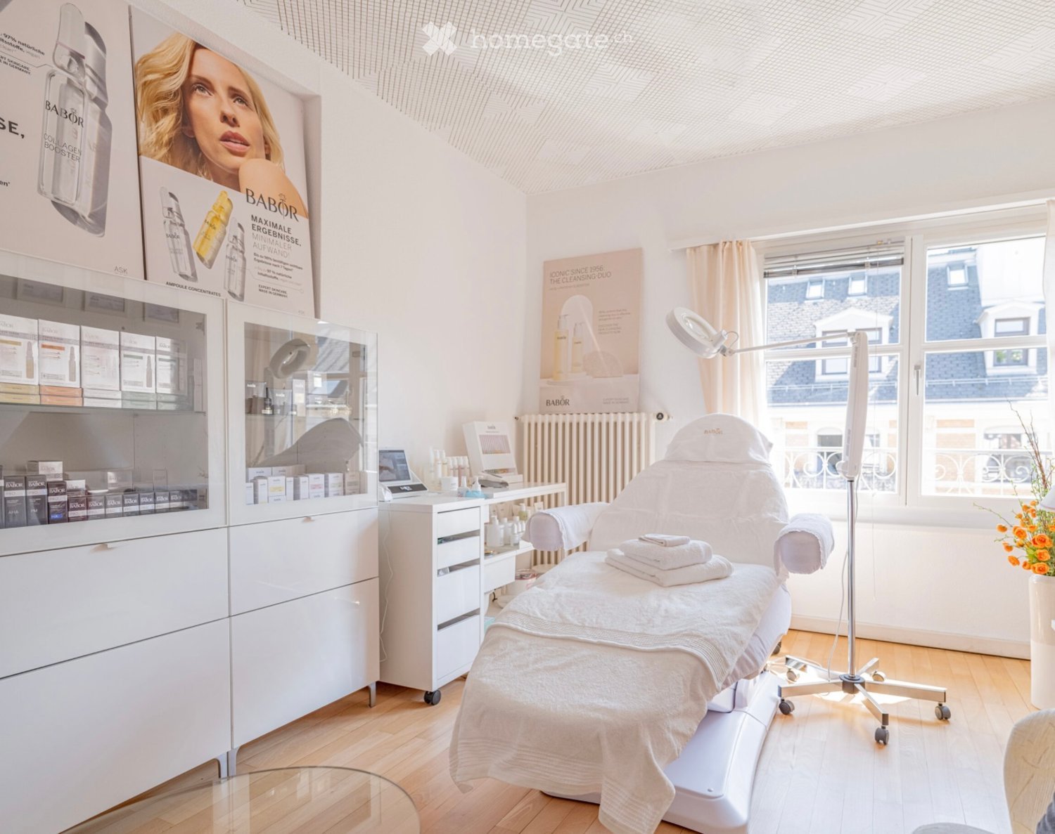Modern treatment room, white walls, wooden floor, medical equipment, examination chair, white cabinets, medical advertisements, window with curtain, exterior view