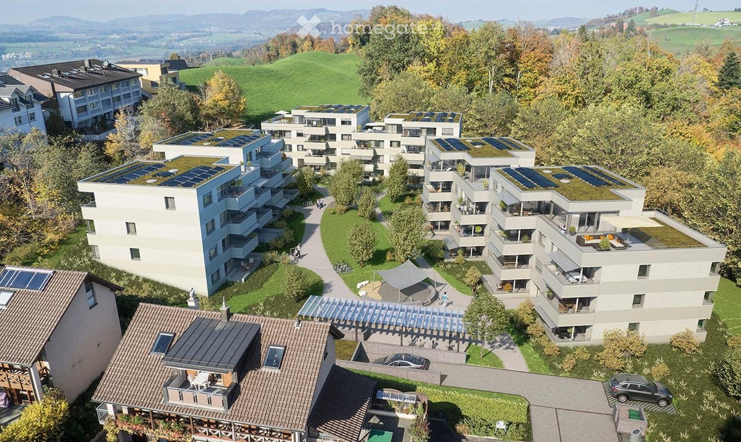Aerial view of a residential complex with multiple buildings, solar panels on roofs, green spaces, and a playground.