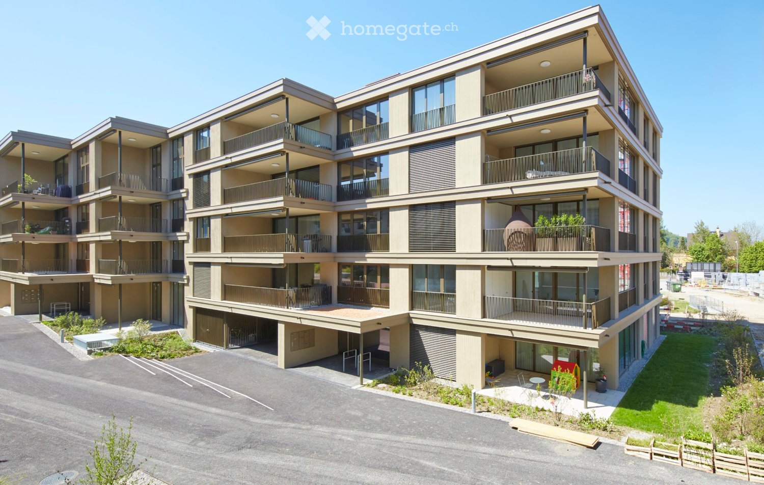 Modern multi-story residential building with balconies, large windows, and a parking area.