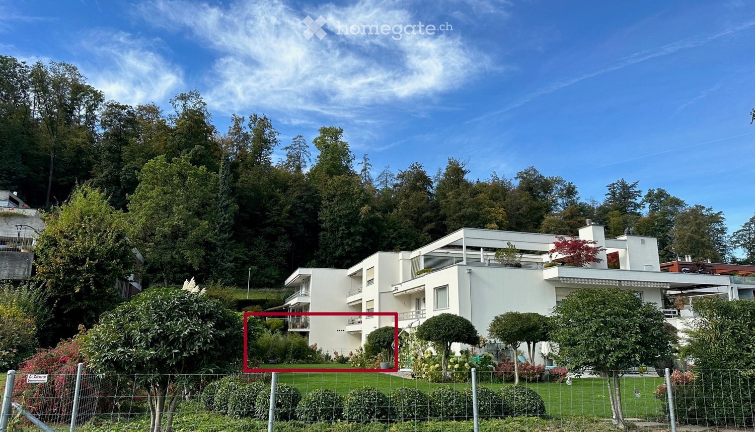 Modern white multi-story building with balconies and terraces, surrounded by lush greenery and trees.