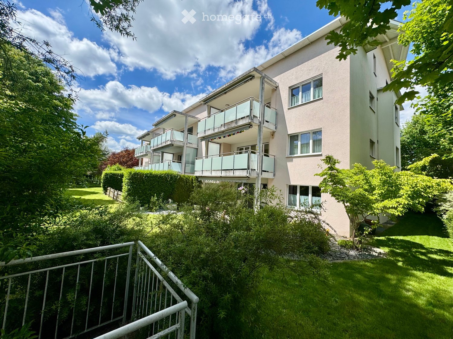 3 story apartment building, white exterior, balconies, green lawn, trees