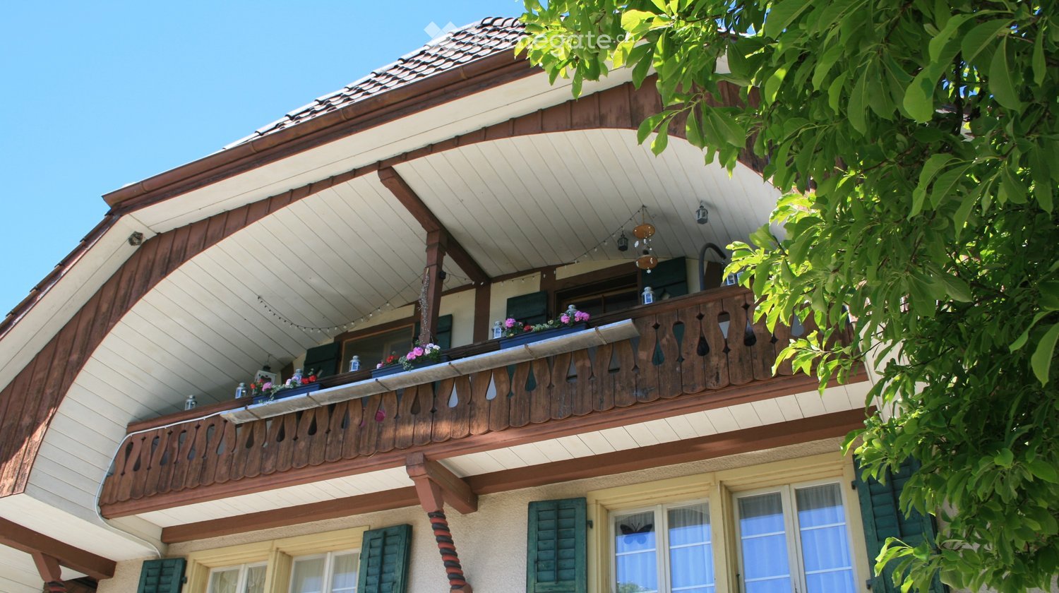 A multi-story building with a wooden balcony, green shutters, and flower boxes on the balcony railing.
