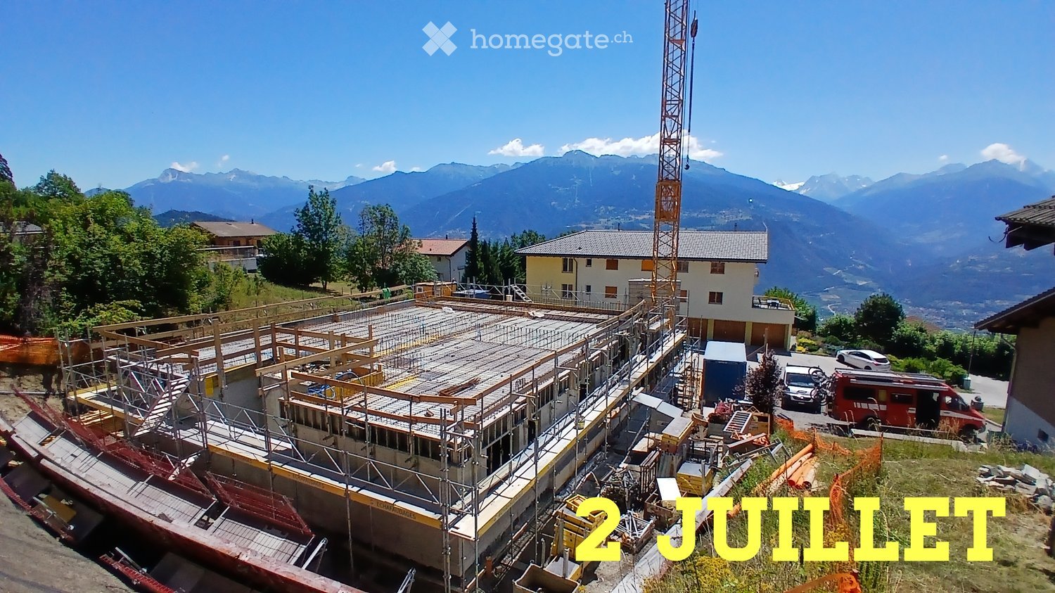 A construction site with scaffolding and a crane, overlooking a mountainous landscape with neighboring houses and vehicles.