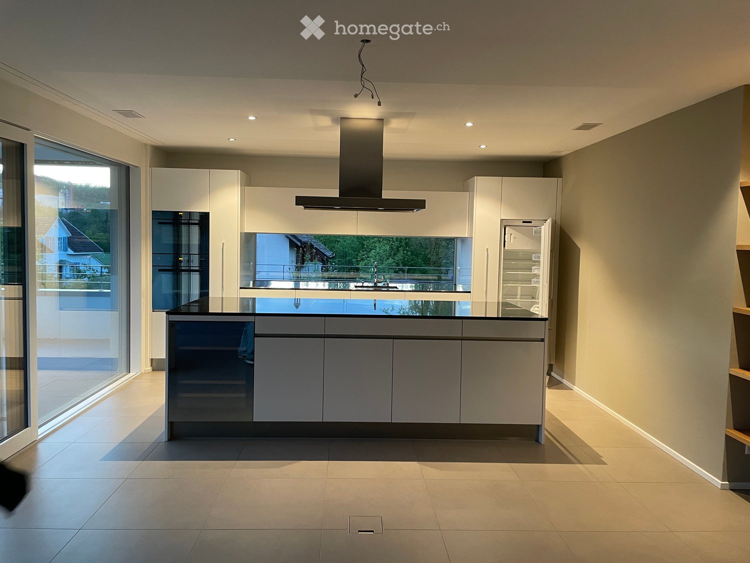 Modern kitchen with white and grey cabinets, a central island, and a large window offering a view of the outdoor area.