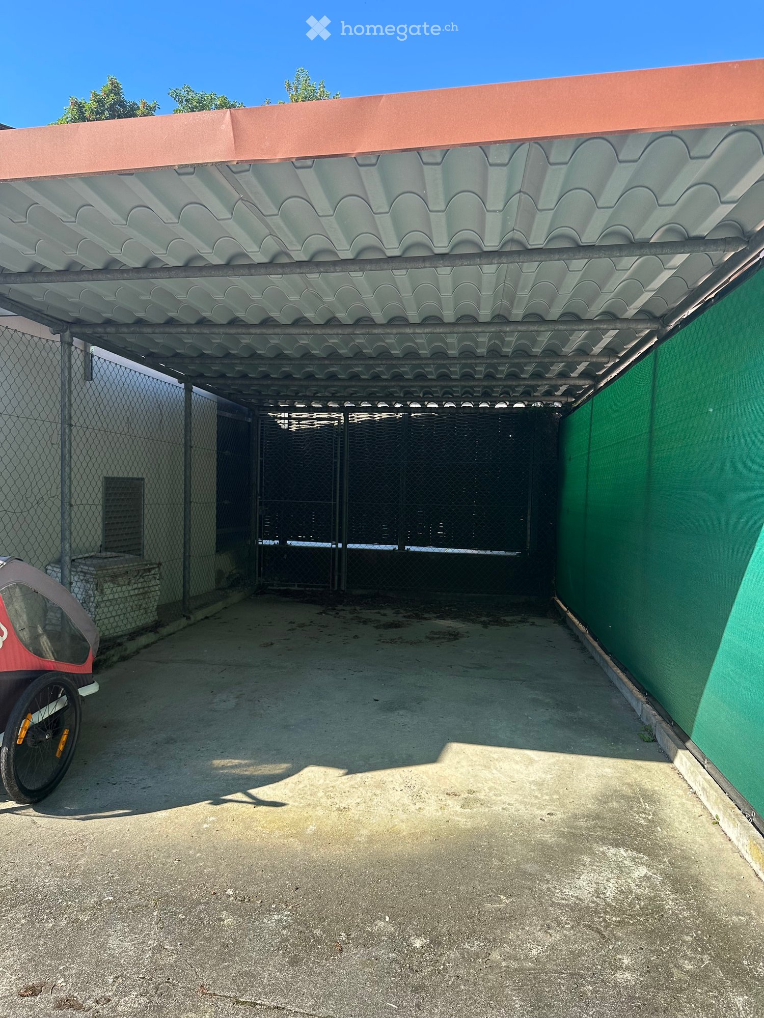 Covered garage area with metal roof structure, chain-link fence, and gated entrance.