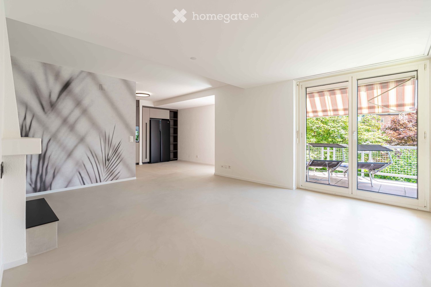Bright, empty room with white walls, large sliding glass doors leading to a balcony, and a modern fireplace with a decorative mural on one wall.