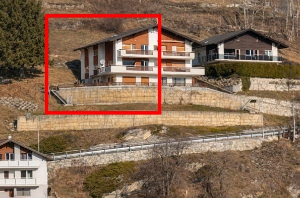 Multi-story residential building on a hillside with balconies and a raised ground floor accessed by stairs.