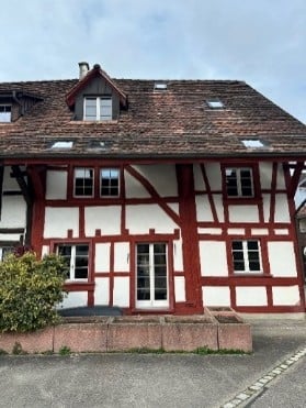 Traditional half-timbered house with red and white exterior, multiple windows, and a pitched roof.