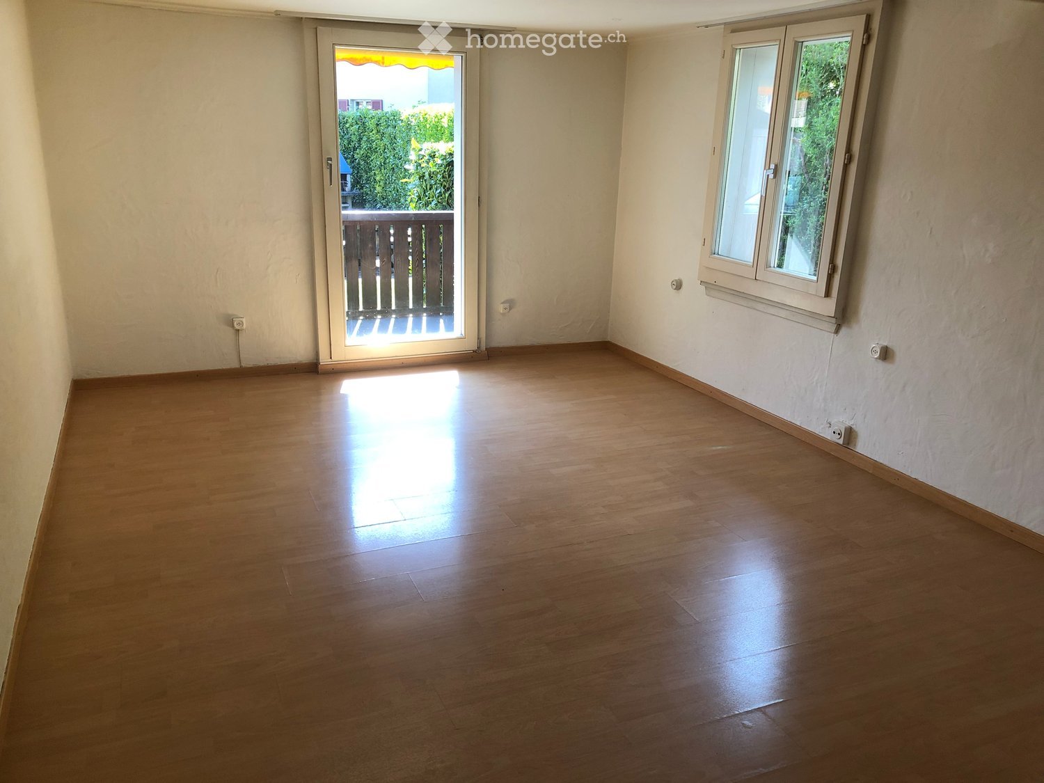 Empty room with wooden flooring, white walls, and a sliding glass door leading to a balcony.