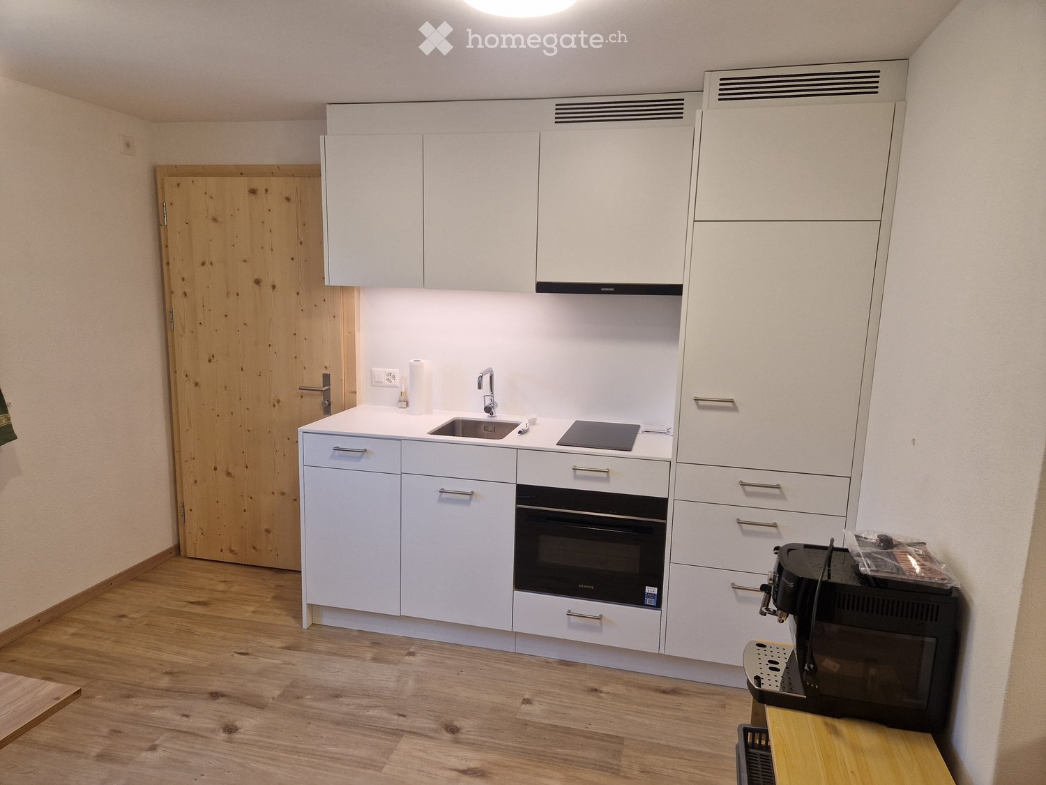 Modern kitchen with white cabinets, a sink, an oven, and a coffee machine on a wooden countertop.
