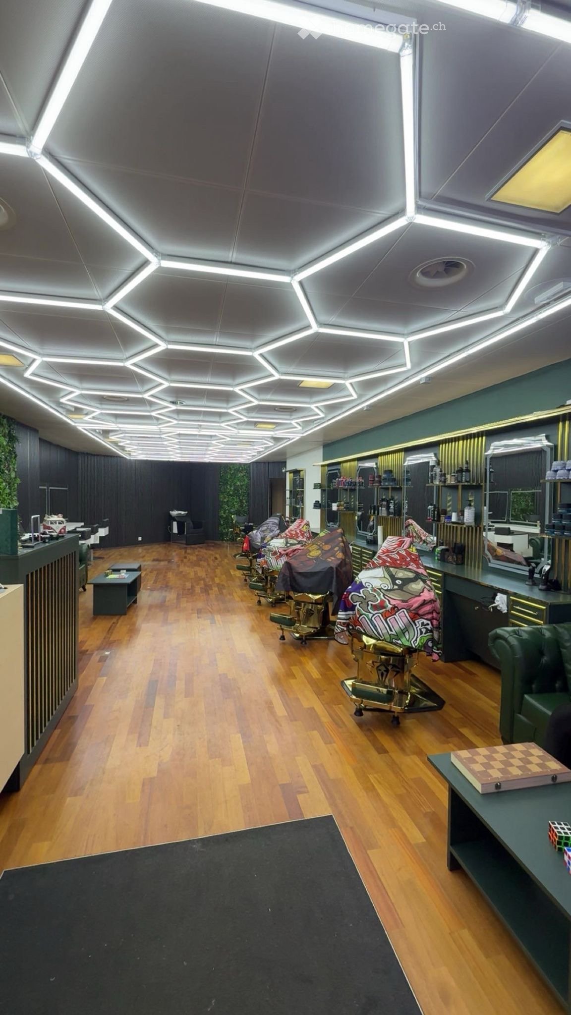 Modern interior with wooden flooring, geometric ceiling lights, and stylish furniture including chairs, tables, and a sofa.