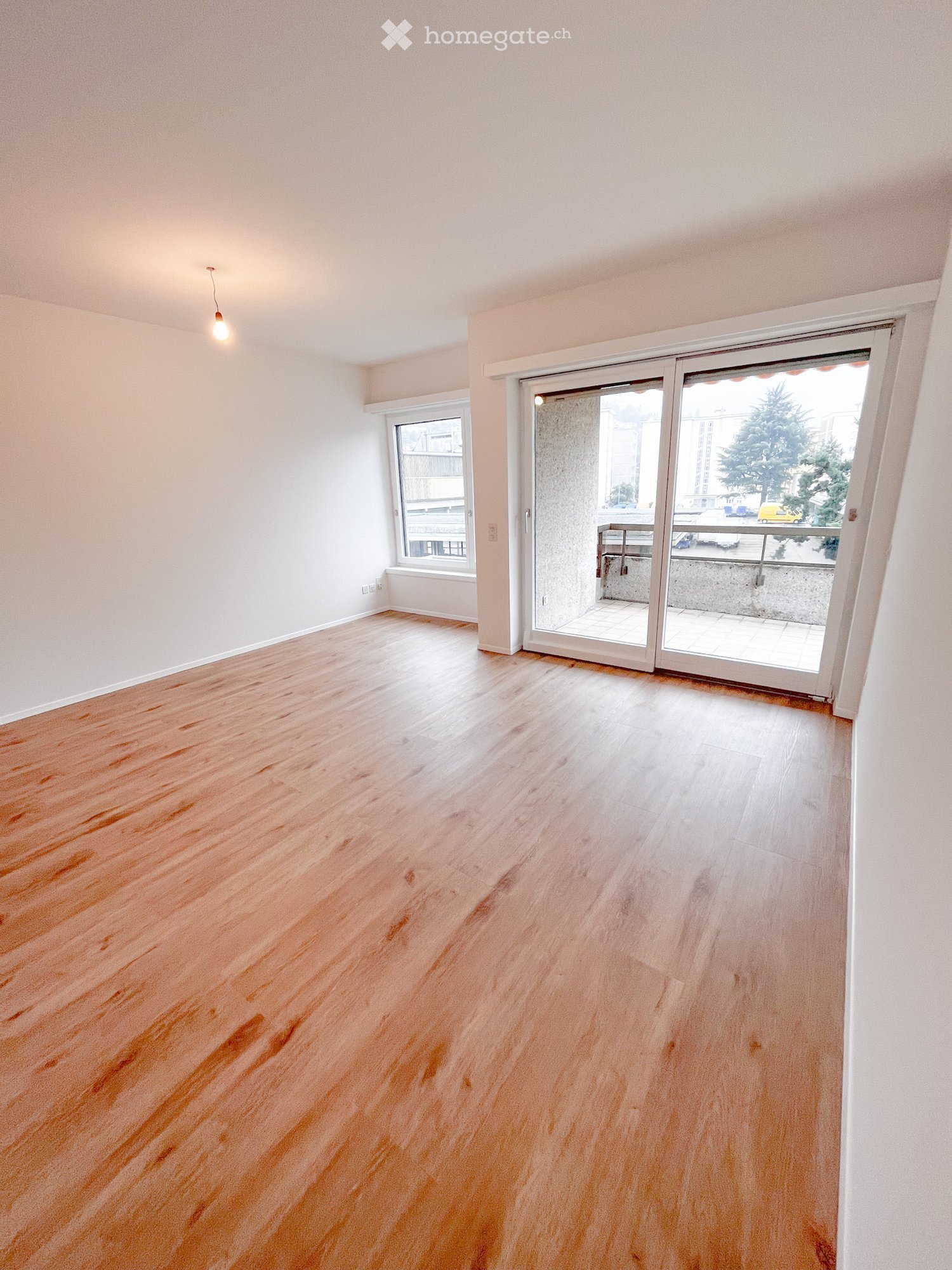 Empty room with wooden flooring, white walls, and large sliding glass doors leading to a balcony.