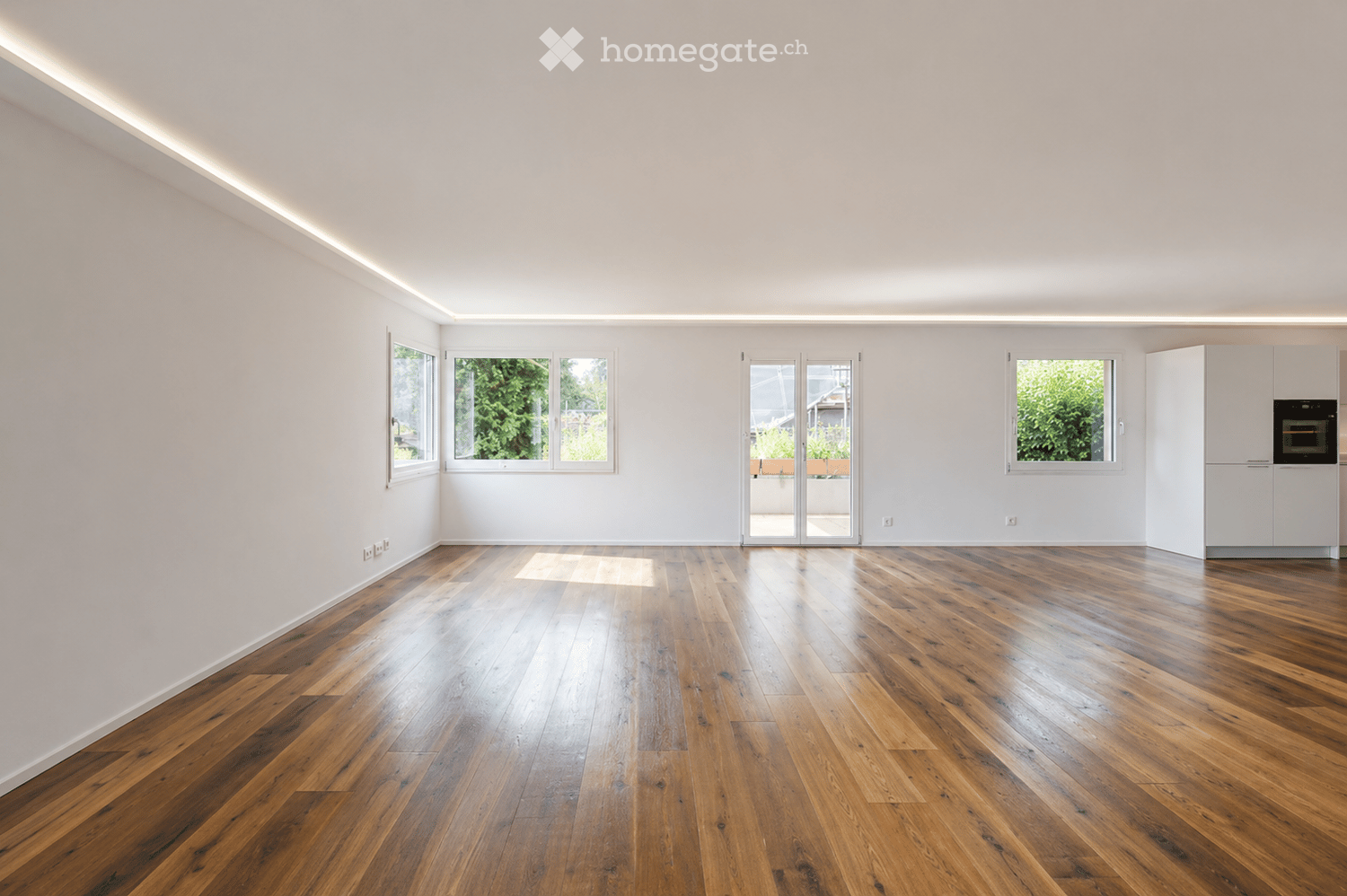 Empty room with wooden flooring, white walls, large windows, and a sliding glass door leading outside.
