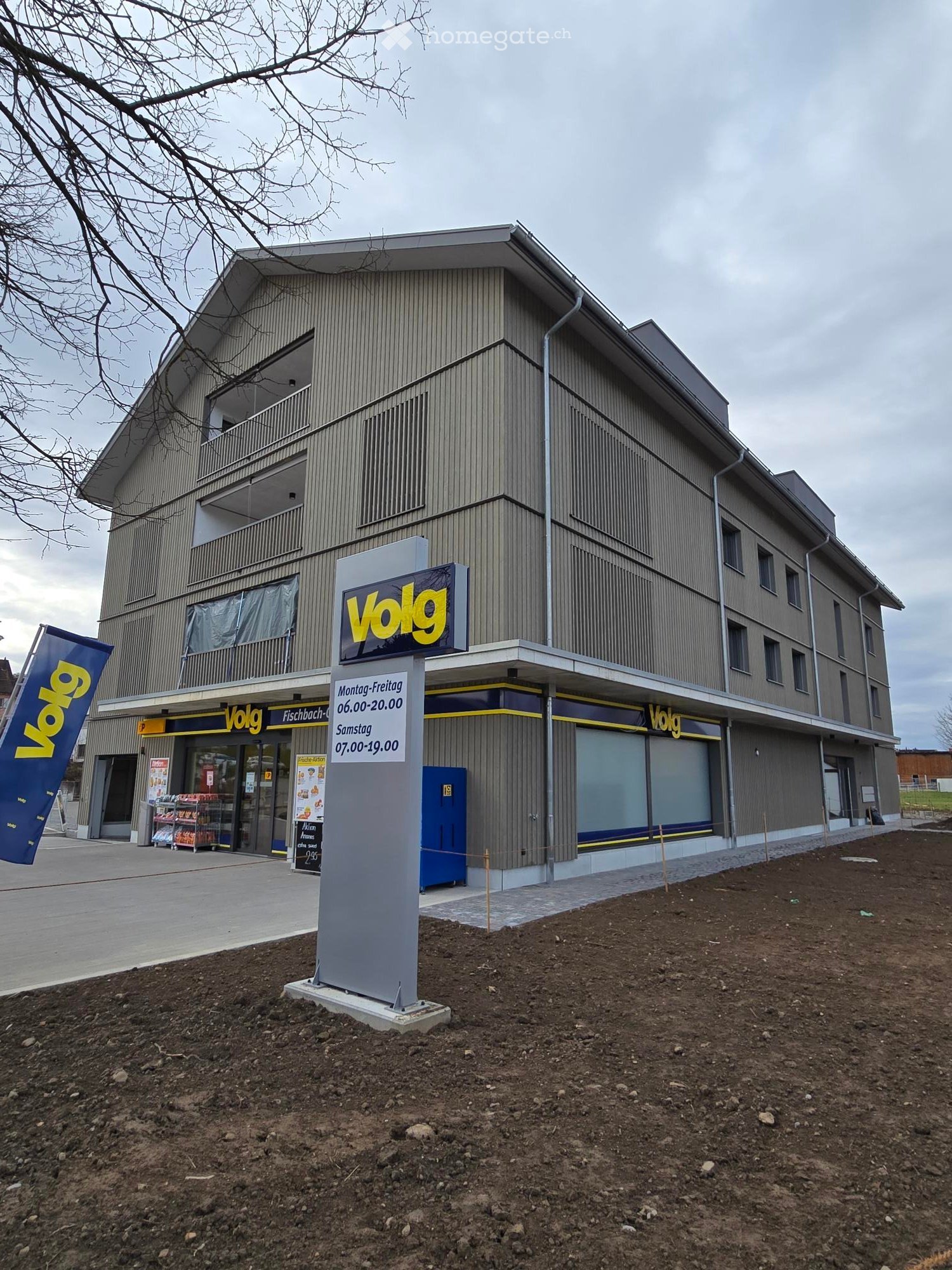 Commercial building with 3 floors, concrete and wooden wall facade, signage for VOLG, front yard
