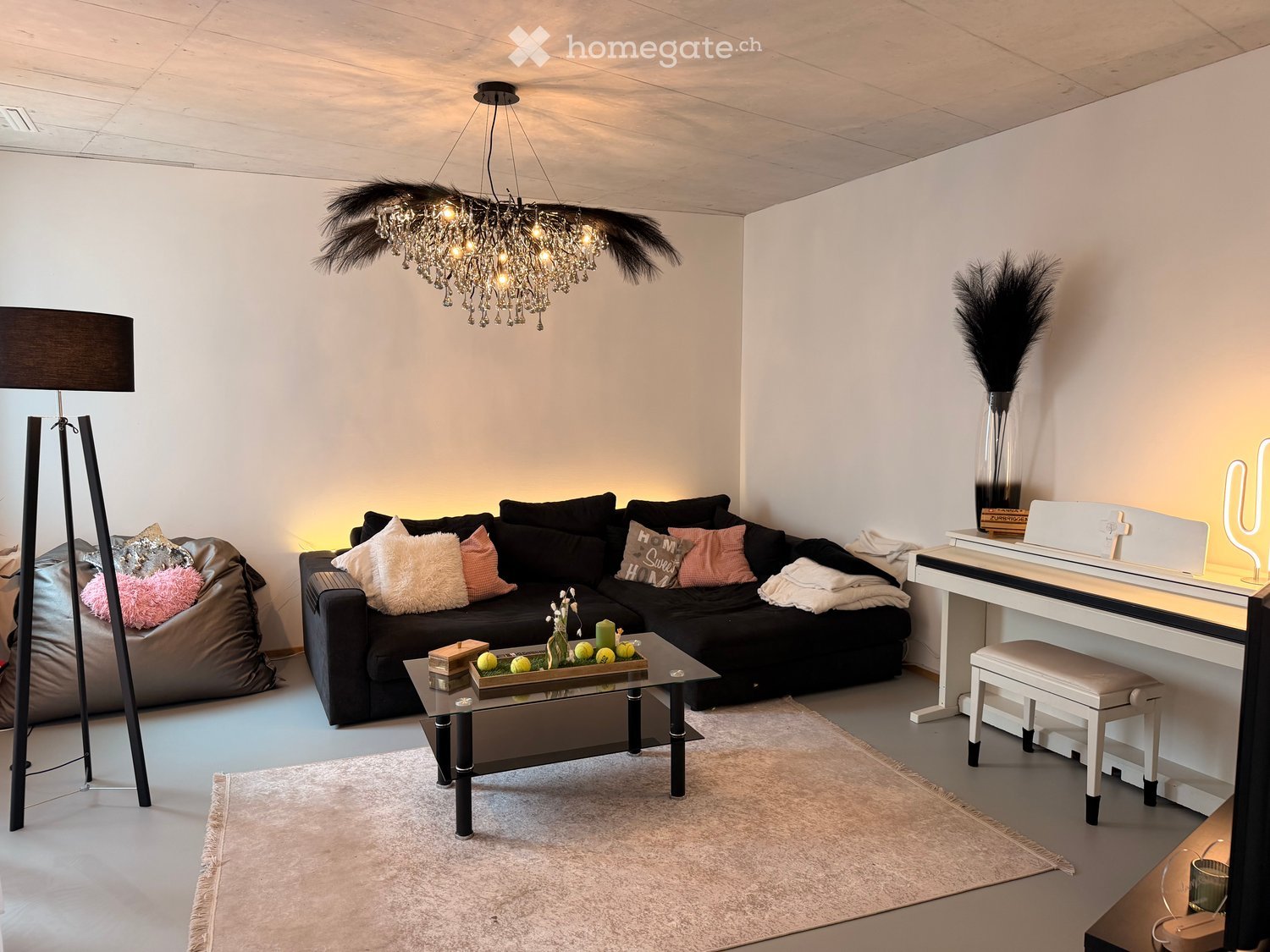Modern living room with a black sectional sofa, coffee table, piano, floor lamp, and decorative items.