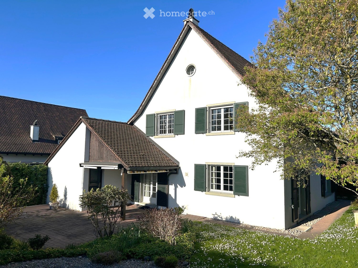 Detached house, white exterior, brown roof, green shutters, small garden, brick driveway, chimney