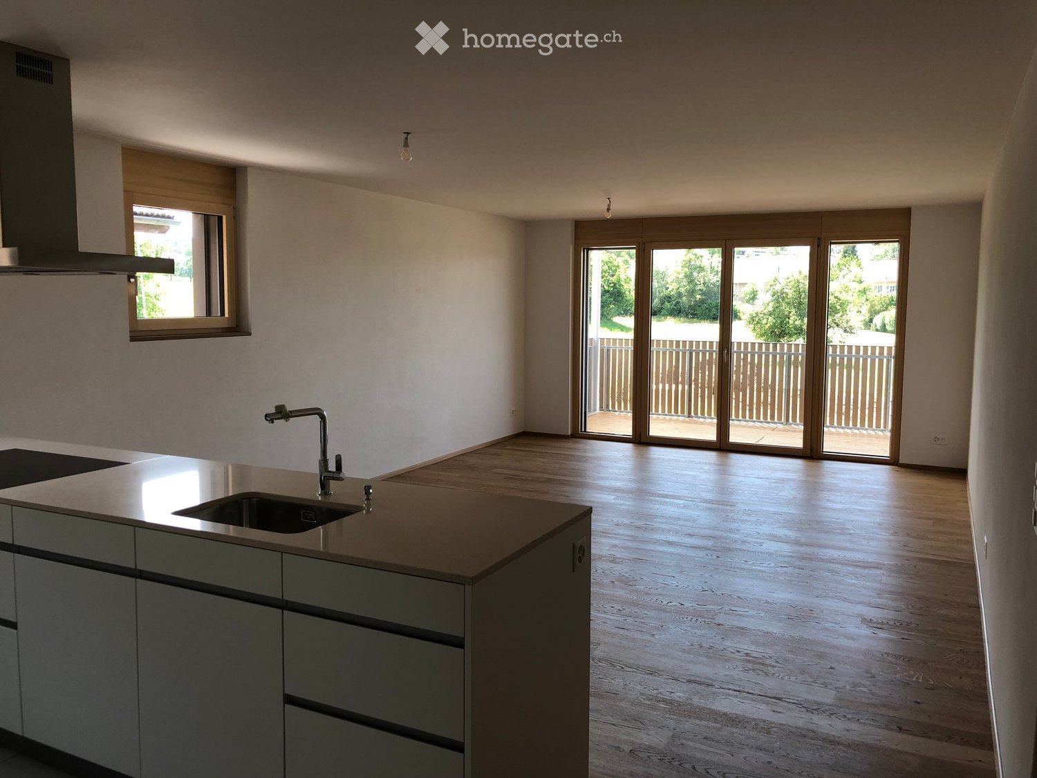 Empty kitchen with modern grey cabinets, a central island with a sink, and large sliding glass doors leading to a balcony.