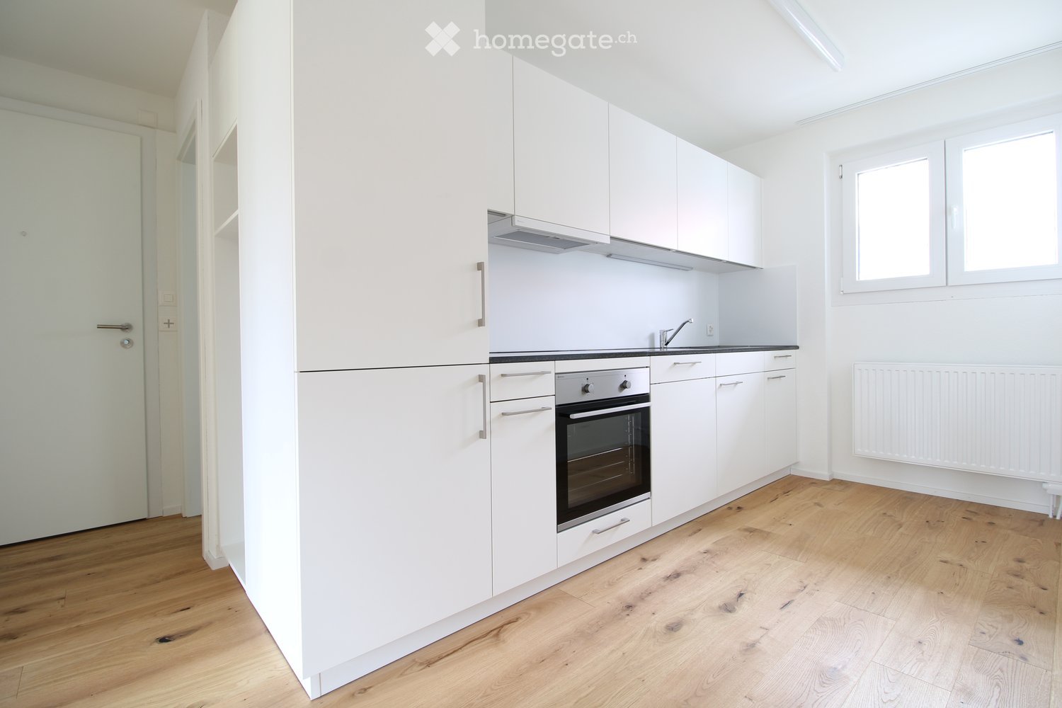 modern kitchen with white cabinets, wooden floor, built-in oven, sink, faucet, windows, white radiator