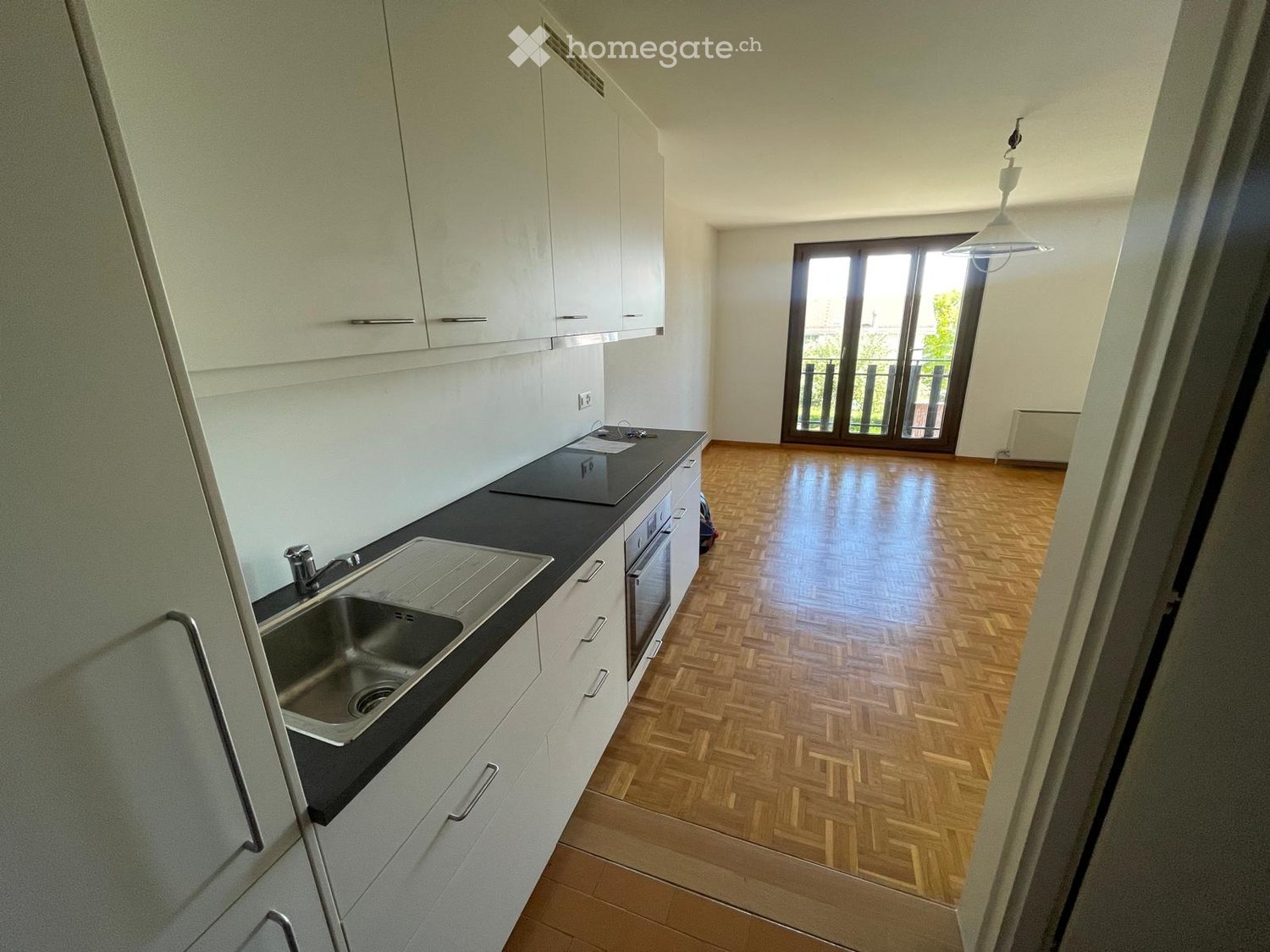 Modern kitchen with white cabinets, black countertop, stainless steel sink, and wooden flooring.