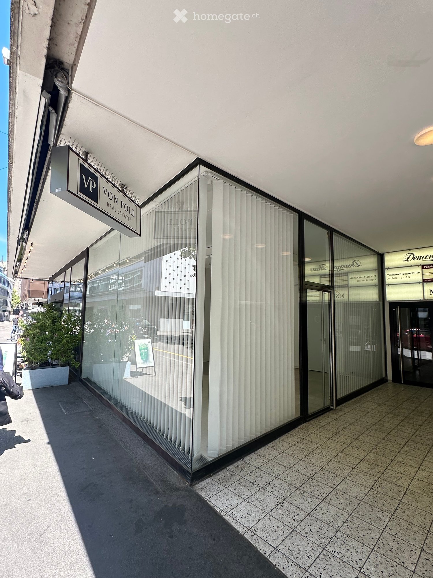 Exterior view of a commercial building with large glass windows, vertical blinds, and a sign reading "VP VON POLLI REAL ESTATES".