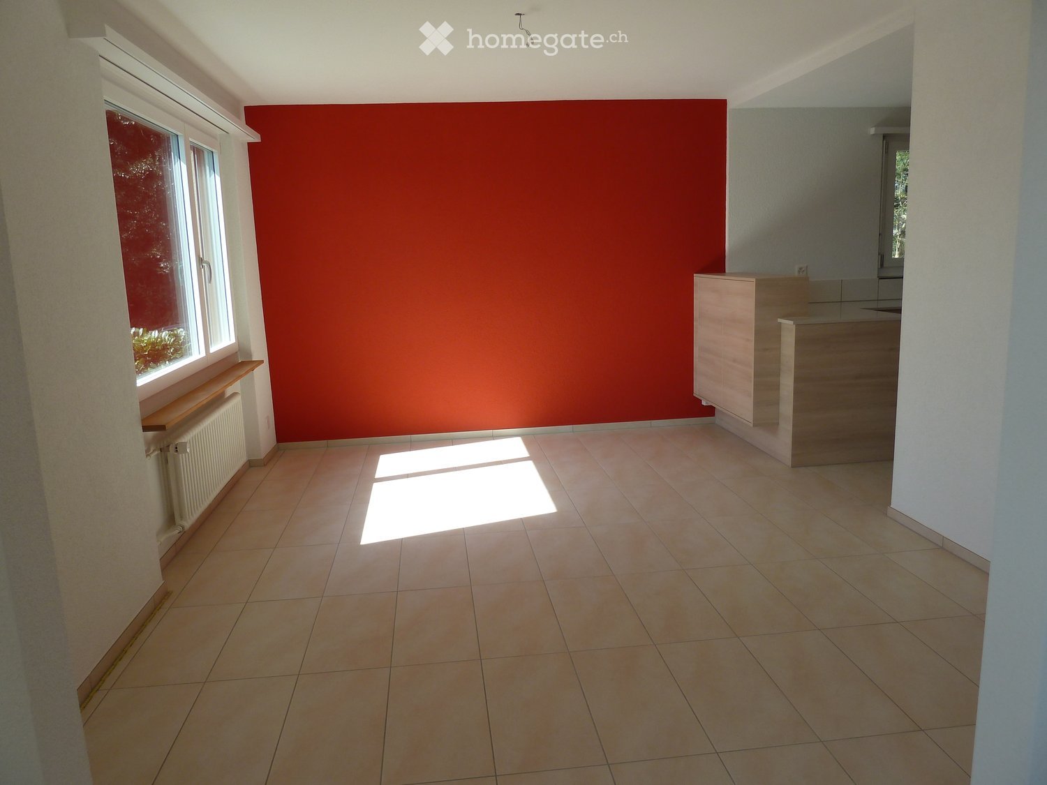 Empty room with tiled floor, red accent wall, window with blinds, radiator, and a small wooden cabinet in the corner.