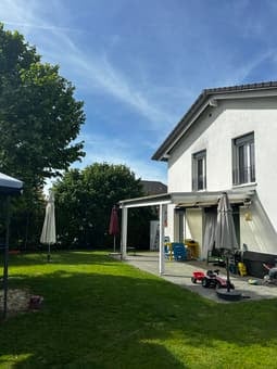 Well-maintained garden with a lawn, patio area, and outdoor furniture including chairs and umbrellas.