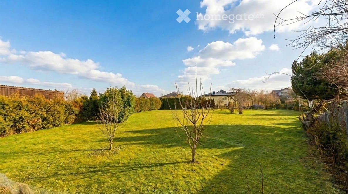 Well-maintained garden with green grass, small trees, shrubs, and a wooden fence in the background.