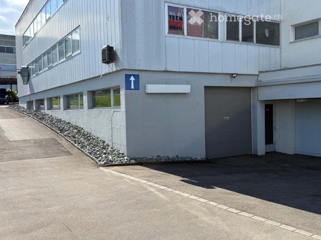 Building. Modern industrial-style building with a raised ground floor, large garage doors, and multiple windows.
