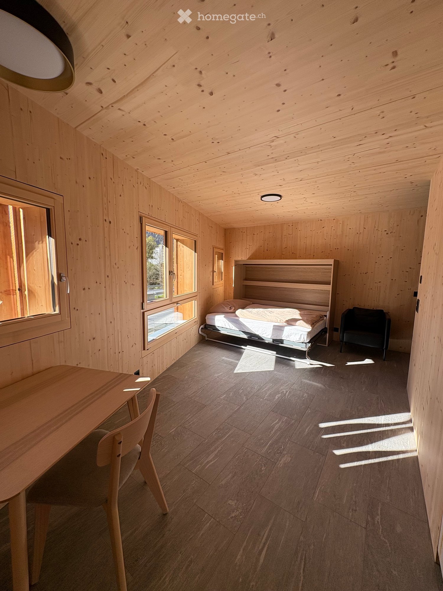 room with wooden walls, wooden floor, bed, chair, desk