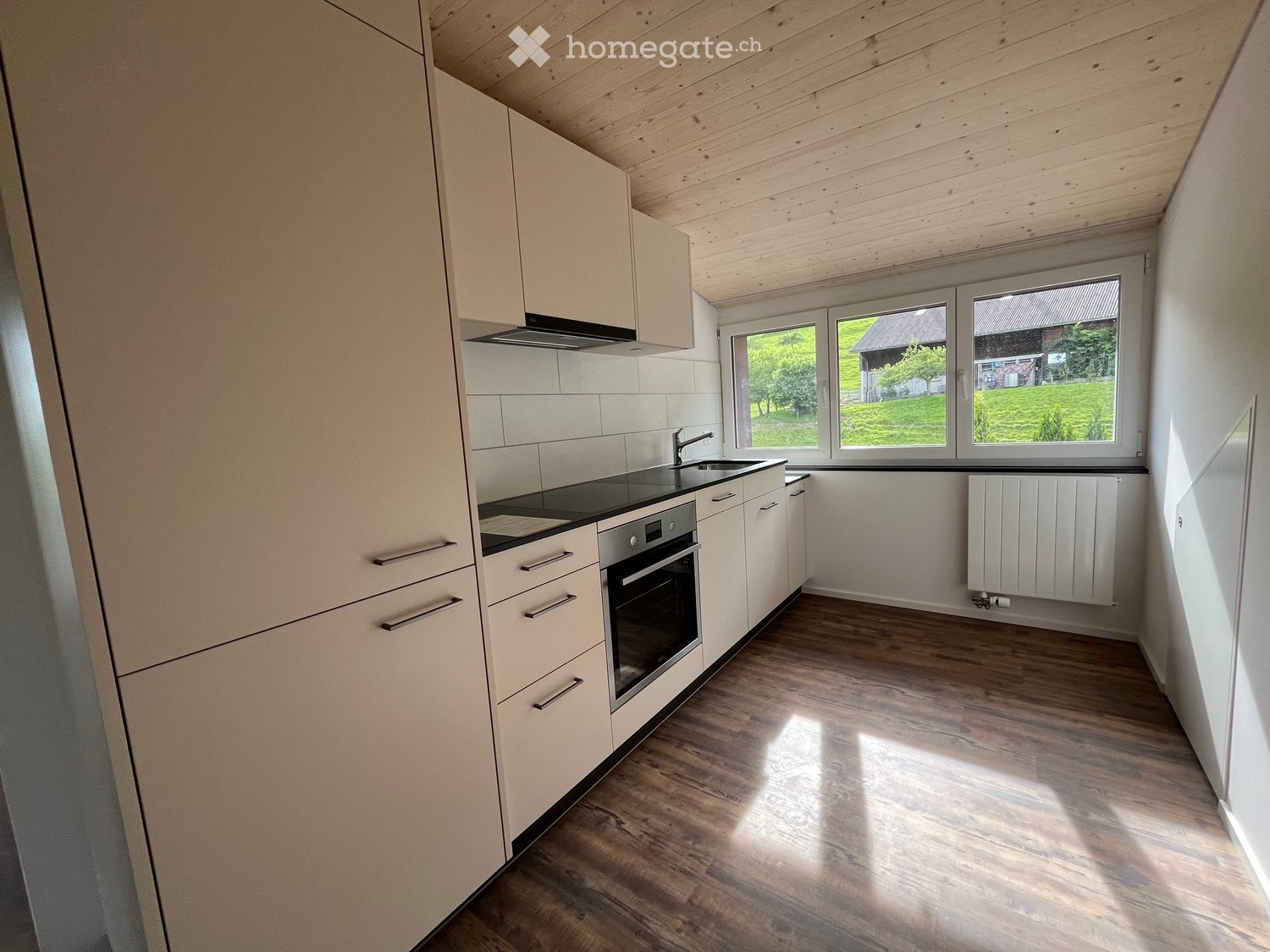 Modern kitchen with white cabinets, wooden floor, and a view of a green field.