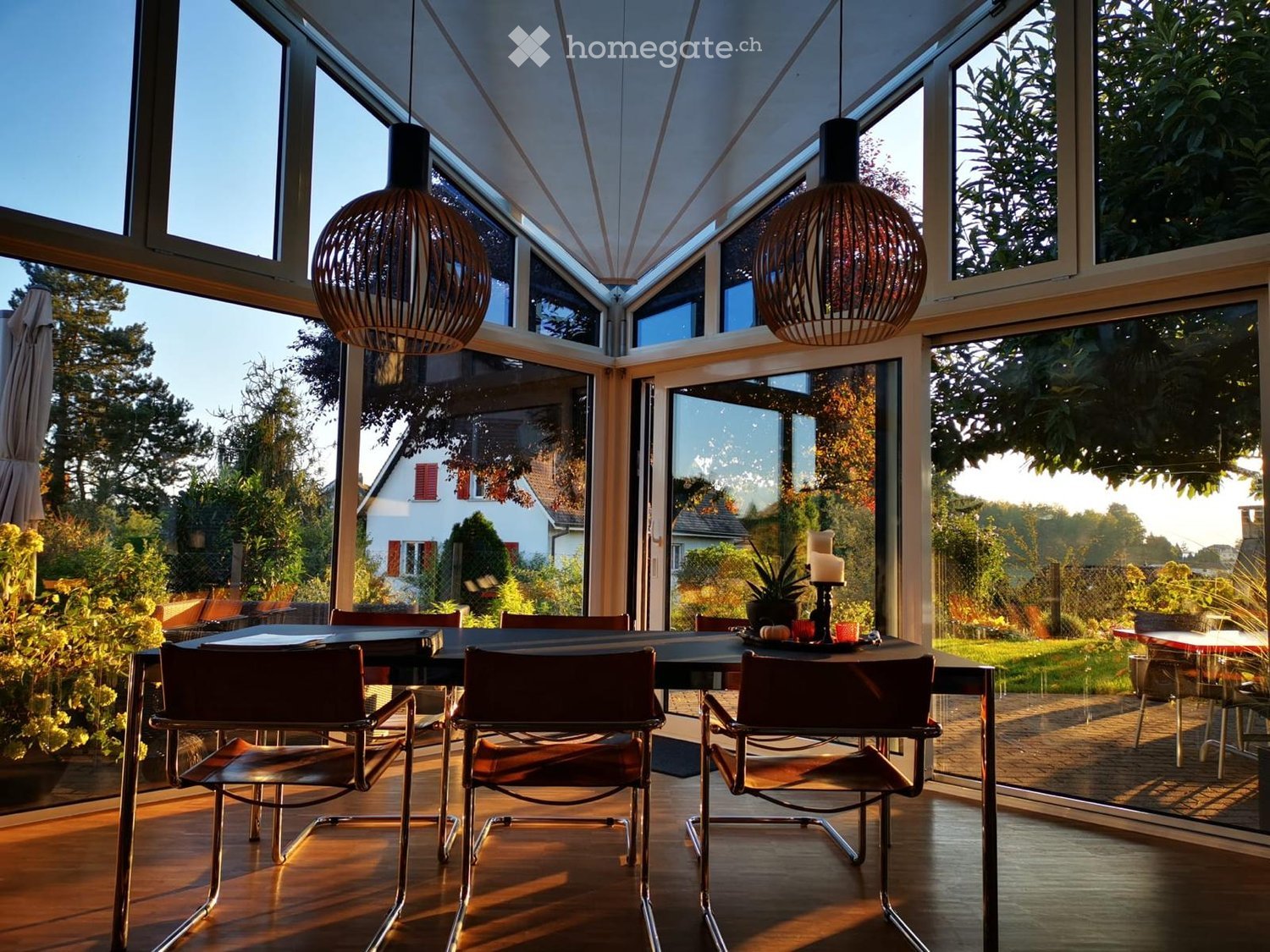 Dining area with large windows, wooden floor, modern chairs, dining table, pendant lamps, and a plant on the table.