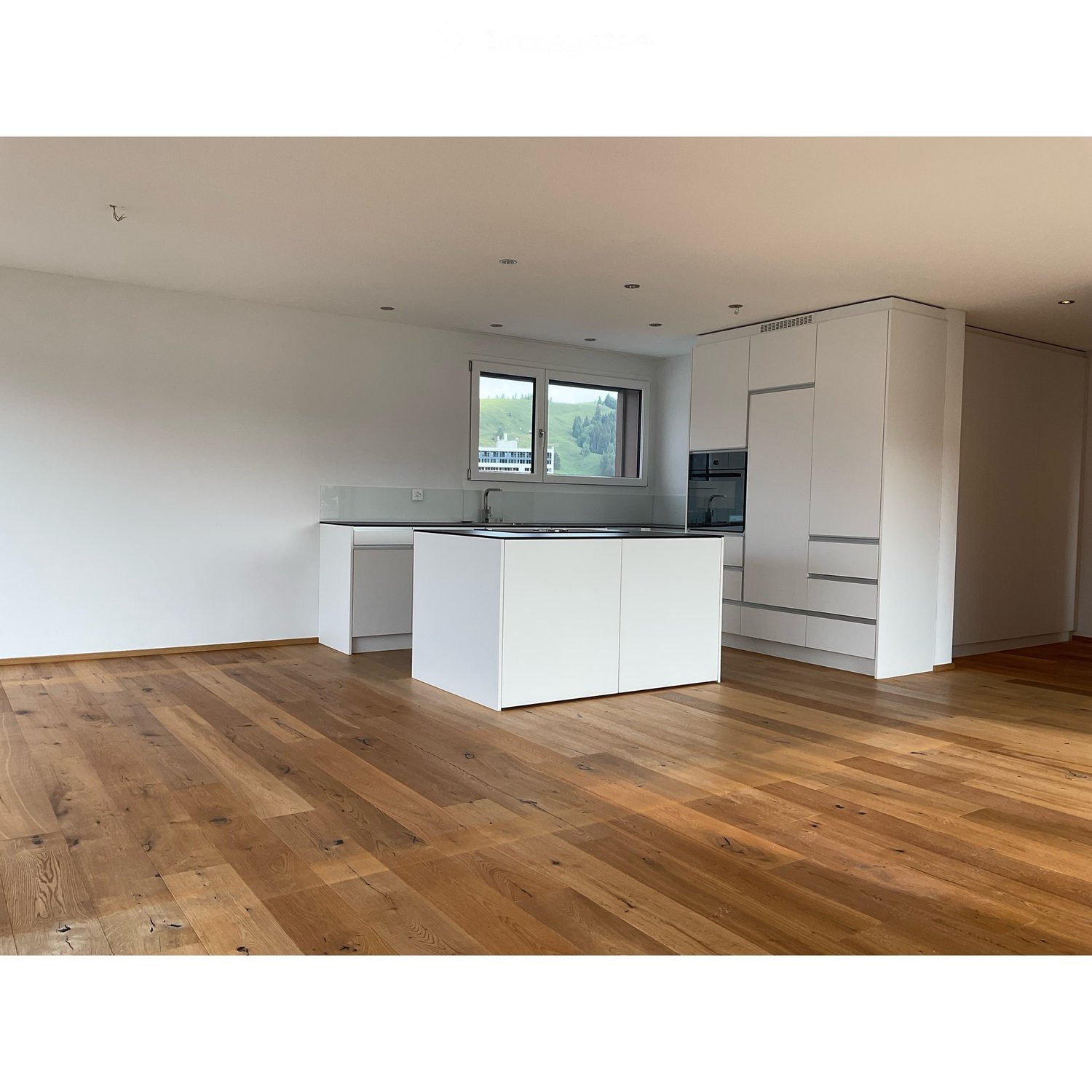 Modern kitchen with white cabinets, a central island, and wooden flooring. Features a large window with a scenic view.