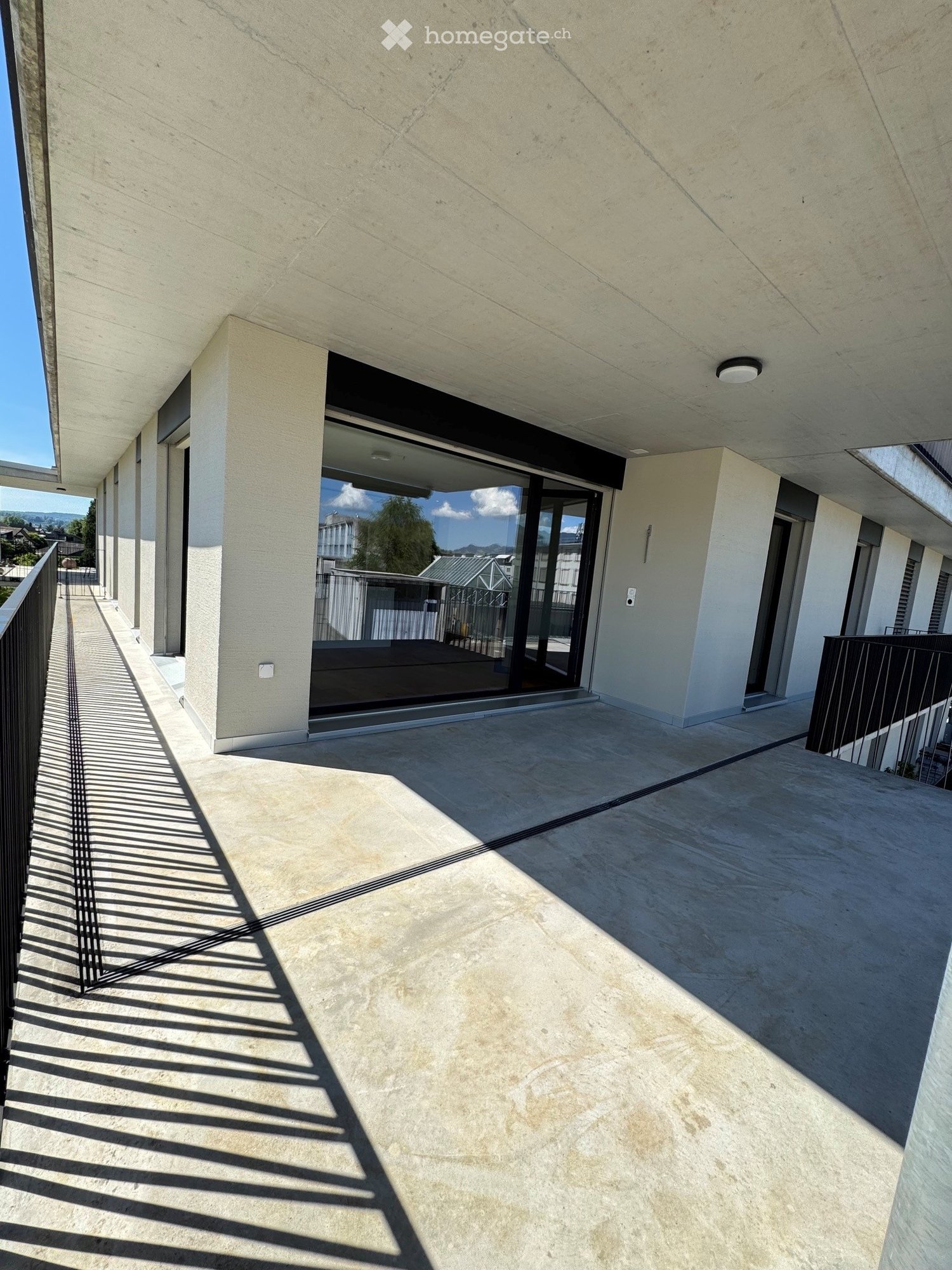 Modern balcony with concrete floor, glass sliding doors, and metal railings, featuring clean lines and ample natural light.