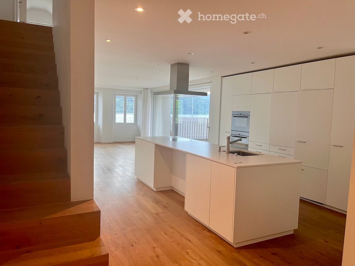Kitchen. Modern kitchen with white cabinetry, a central island, and a stainless steel sink and oven. The space features wooden flooring and large windows with white curtains.