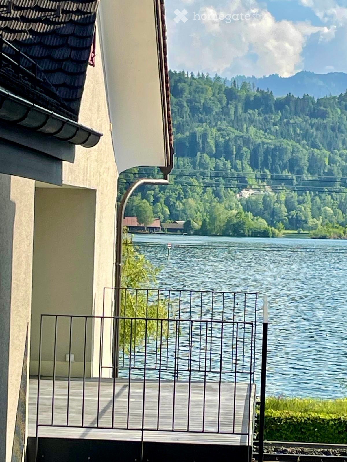 Balcony / Terrace. Balcony overlooking a serene lake with surrounding greenery and distant mountains.
