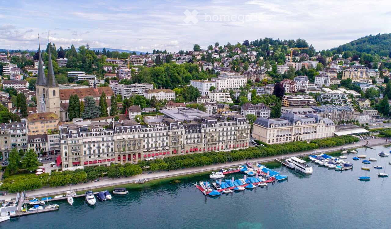 Aerial view of a cityscape with a waterfront, featuring hotels, a casino, a church, and numerous boats docked along the shore.