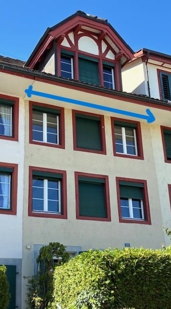A multi-story residential building with a classic facade, featuring multiple windows with shutters and a decorative roofline.