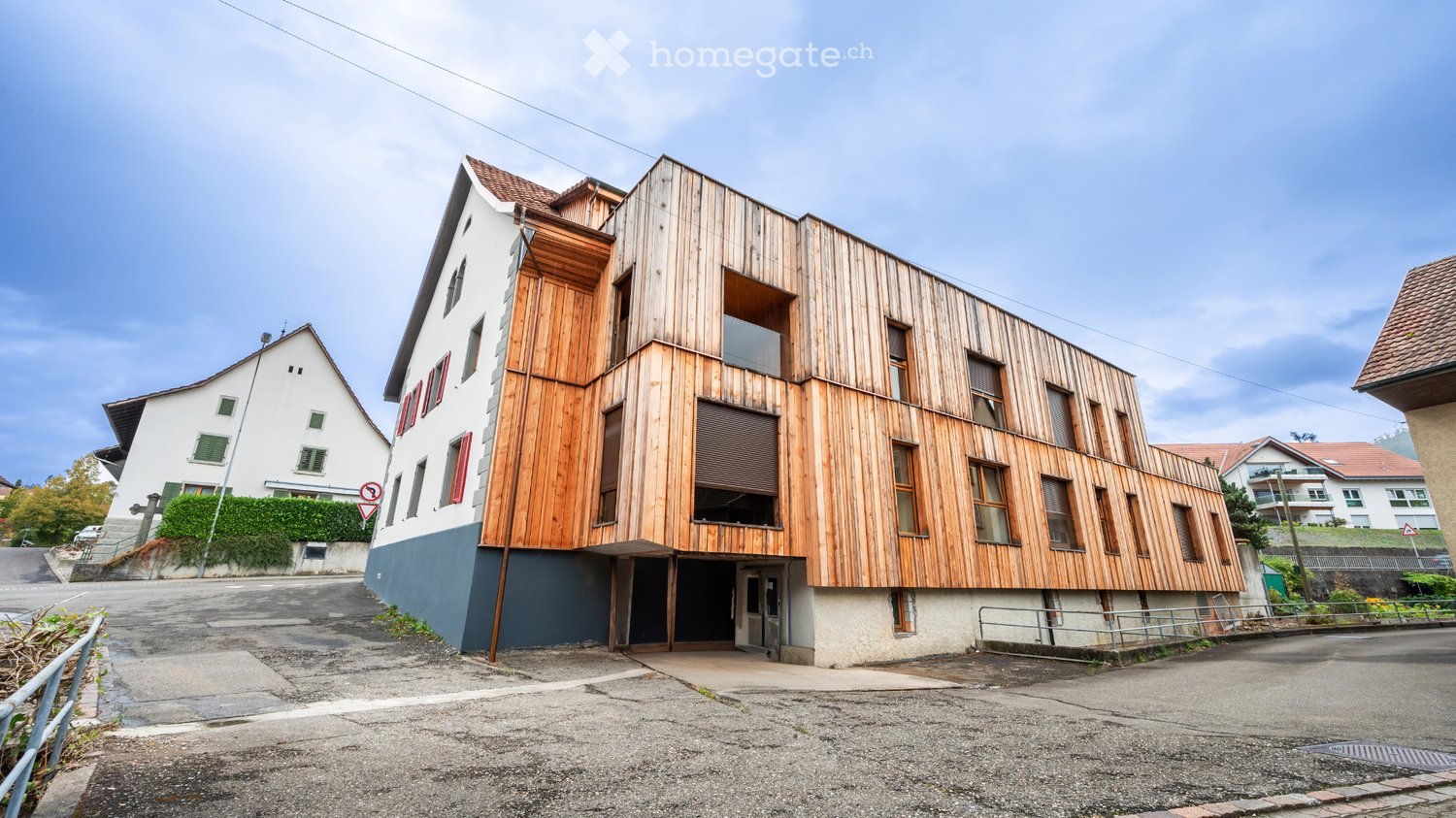 Modern two-story building with wooden facade and blue base, featuring large windows and a covered entrance area.