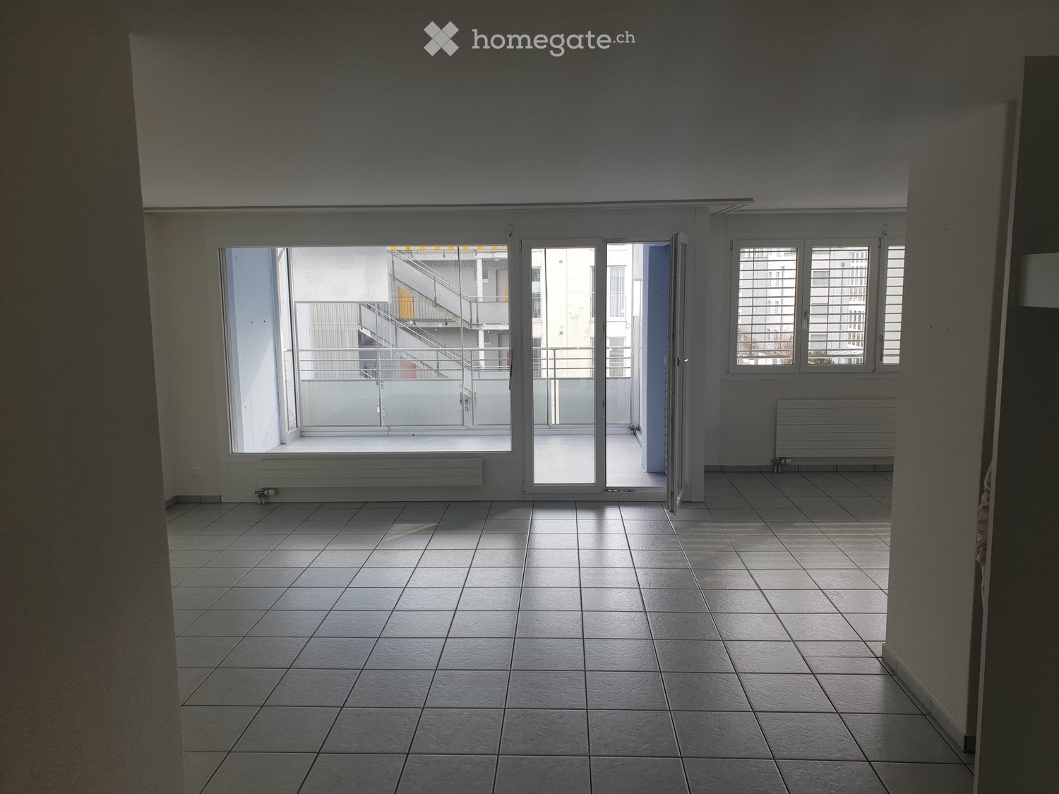 Empty room with tiled floor, large windows, and a balcony access door. No furniture or equipment present.