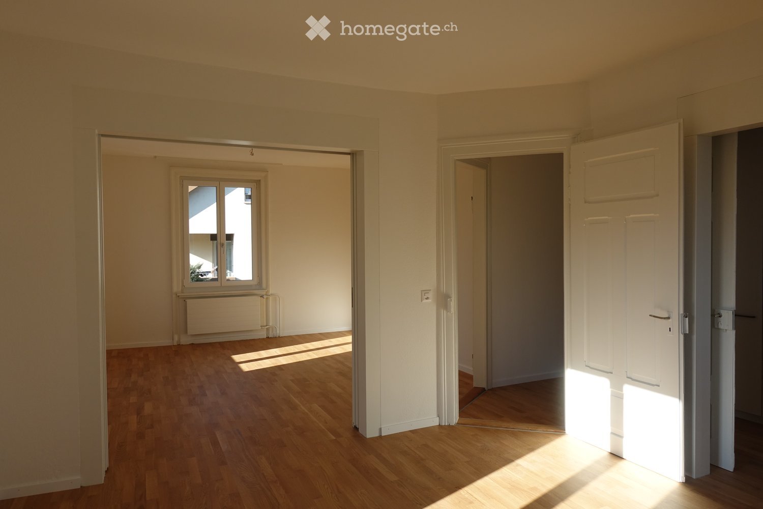 Empty room with wooden flooring, white walls, and a window letting in natural light. No furniture or equipment is present.