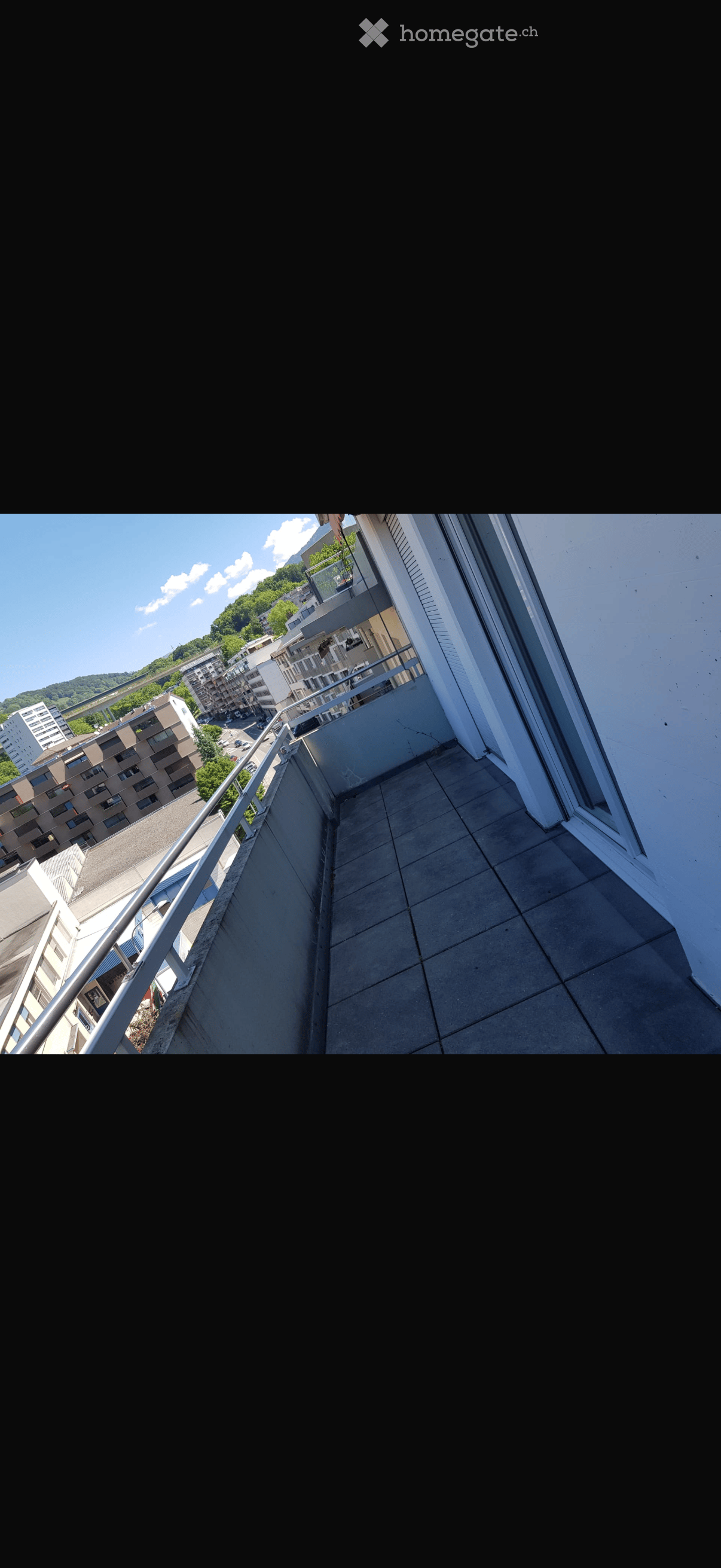 Balcony with tiled floor, metal railing, overlooking a cityscape with buildings and greenery.