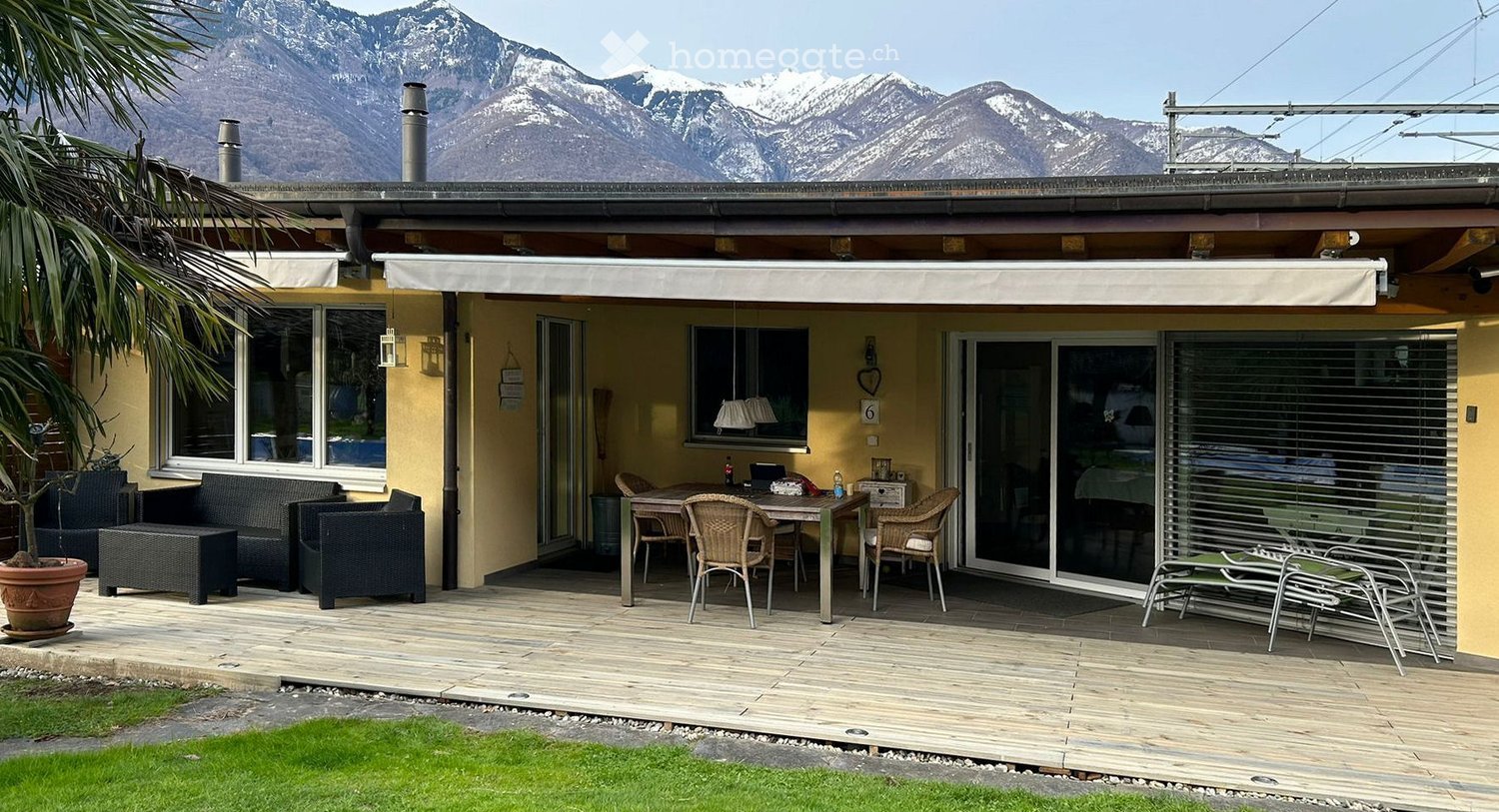 Wooden deck with outdoor furniture including a sofa, ottoman, chairs, and a table, overlooking a mountain view.