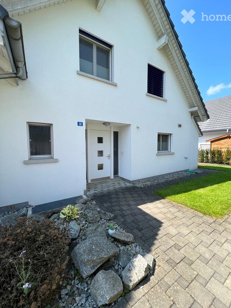White house, modern design, entrance with white door, brick pathway, small garden with green grass, rocks and plants